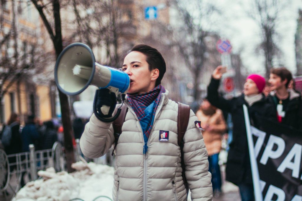 Olga Shevchenko går i ett demonstrationståg. Hon använder en megafon. I bakgrunden syns fler demonstranter.