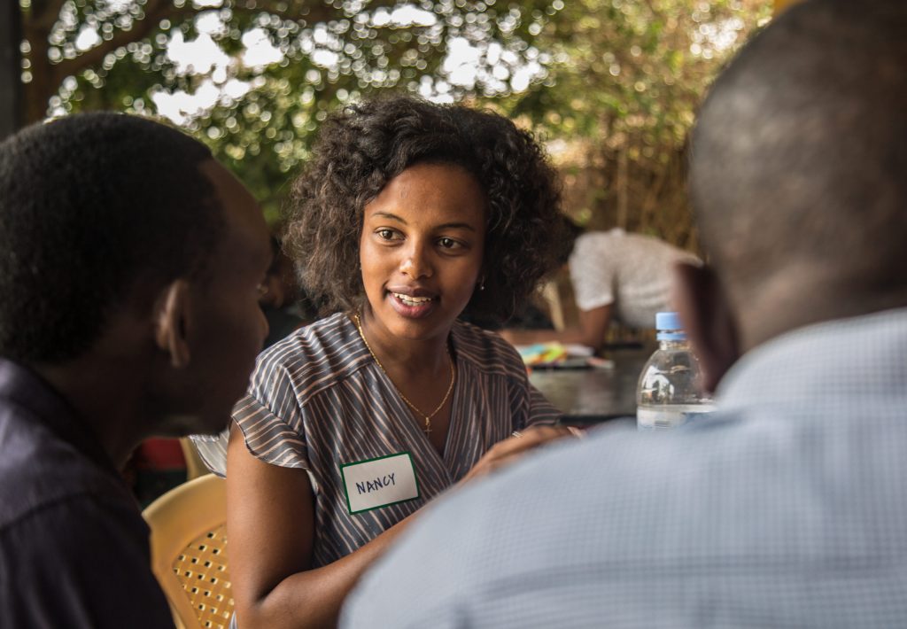 En kvinna med namnskylten Nancy sitter vid ett bord och pratar med två män.
