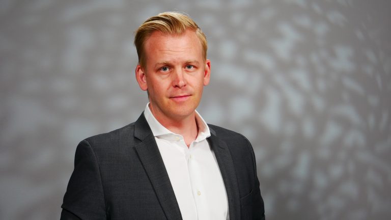 En man i kavaj framför en grå bakgrund.